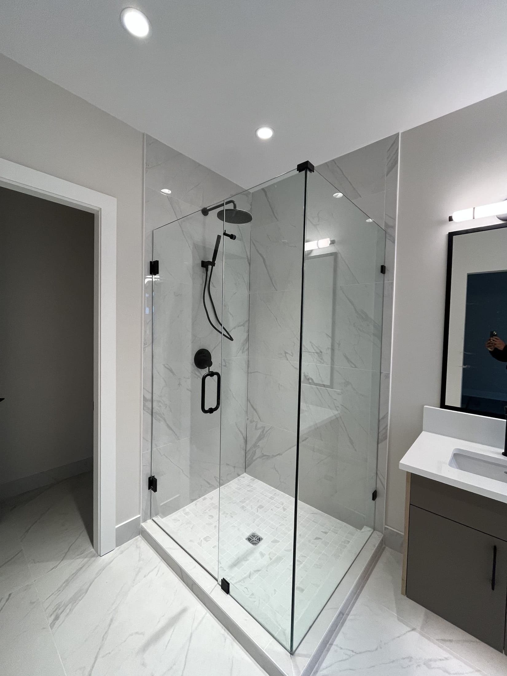 Frameless corner glass shower enclosure with matte black hardware and marble-look tile