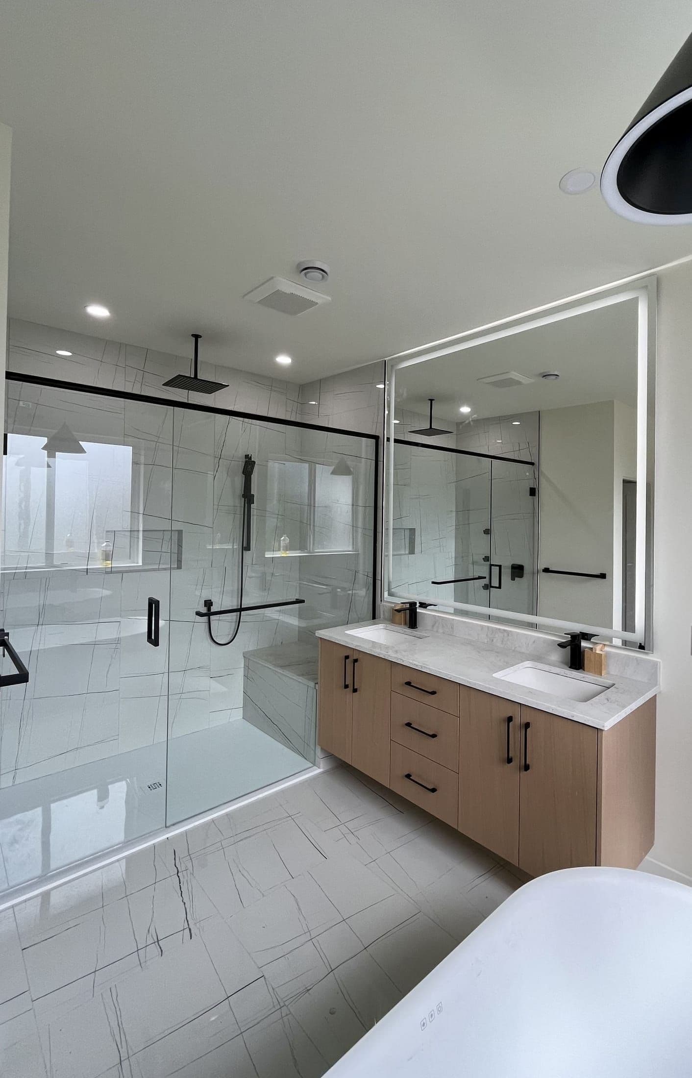 Black-framed glass shower enclosure beside a large LED vanity mirror in a modern master bathroom